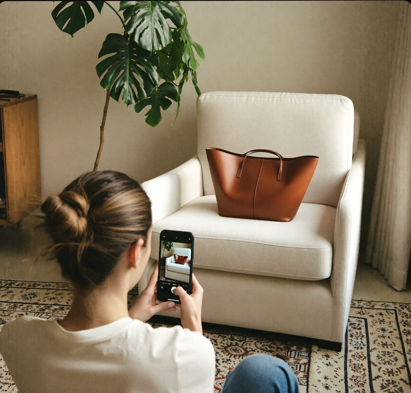 A seller photographing a leather bag on an armchair with their phone